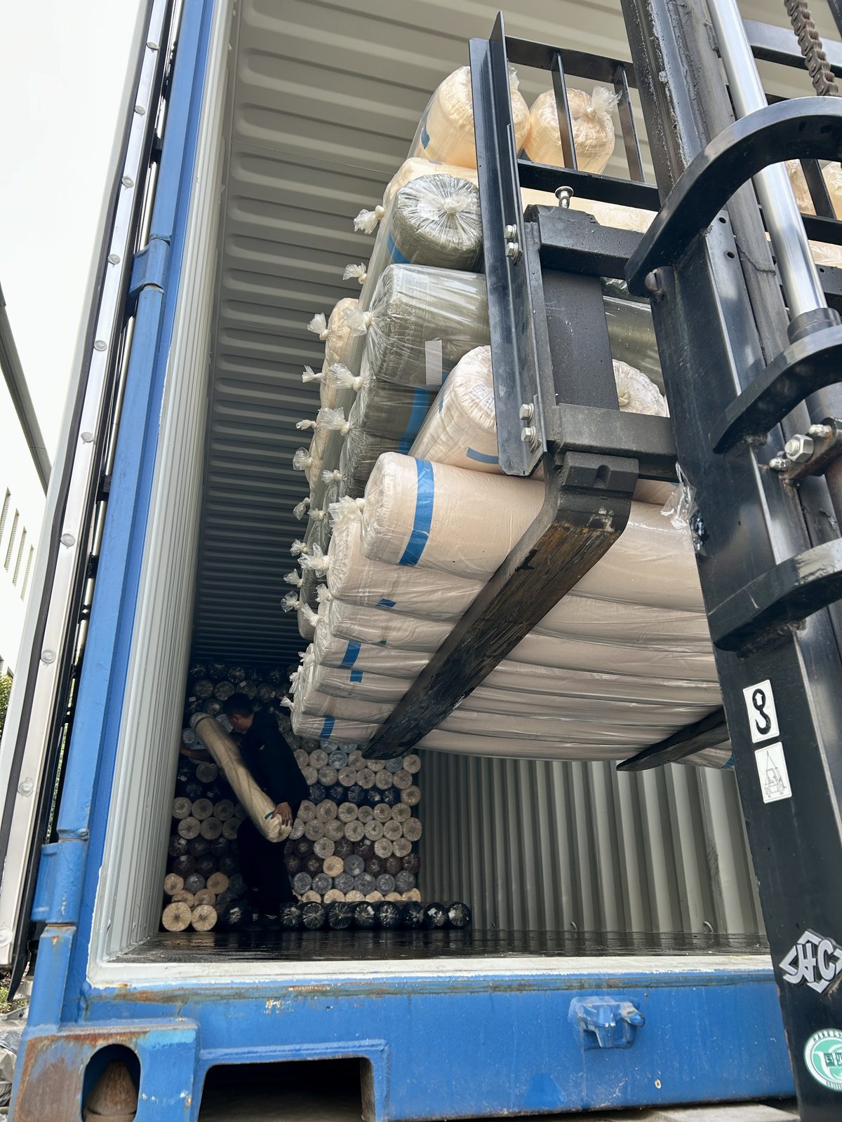 Workers loading fabric rolls into a container